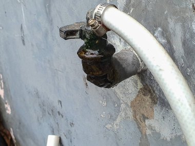 Hortumu bağlı açık su musluğu, sızıntı, hava durumu ve mineral birikimi belirtileri gösteriyor..
