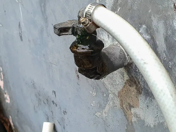 Hortumu bağlı açık su musluğu, sızıntı, hava durumu ve mineral birikimi belirtileri gösteriyor..