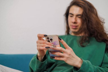 Evde arka planı bulanık cep telefonunu kullanan ikili olmayan biri. Uzun tırnaklar.