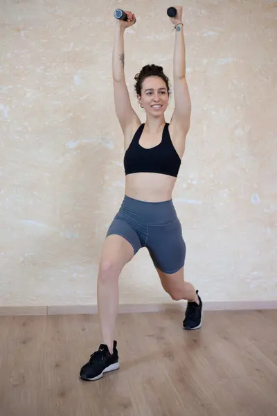 Sağlıklı genç bir fitness kadınının uzun bir portresi halterlerle egzersiz yapıyor.