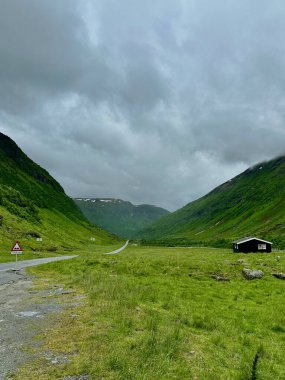 Norveç 'in yeşil yaz dağları arasındaki kahverengi Norveç milli barakası Hitta, yol ve yol işaretleri dağların arasından geçer.