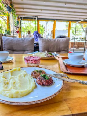 Restoranda öğle yemeği. Rus usulü patates püresi ve otlu biftek köftesi. Arka planda pancar ve ringa balıklı salata, bir fincan kahve ve kafenin içi.
