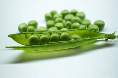 Taze taze bezelyelerin yakın plan görüntüsü, temiz beyaz bir yüzeye serpiştirilmiş bezelyeler ve bezelyeler ortaya çıkarmak için bir kabuk açıldı..