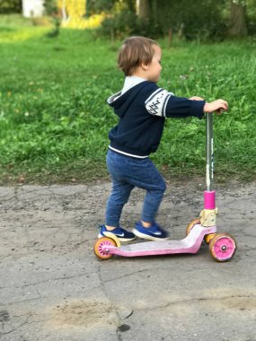 Parkta motosikletli bir çocuk. Güneşli bir günde küçük bir çocuk mobilete biniyor. Anaokulu öğrencileri için aktif spor.