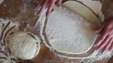Evde pizza yapmak. Hamuru yuvarlıyor, un serpiyor.