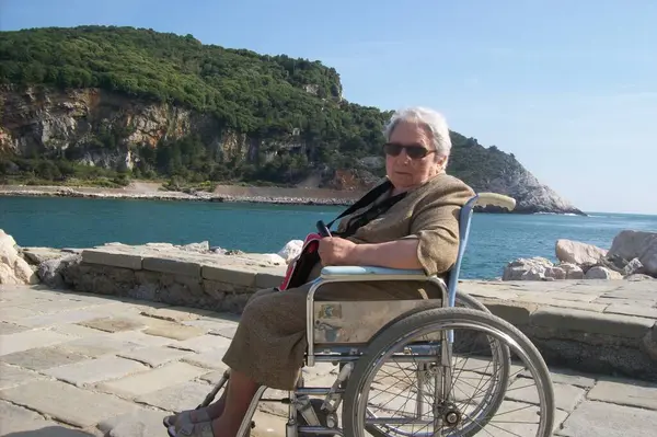 stock image Elderly woman in a wheelchair on the seashore on a sunny spring day. Disability inclusion concept