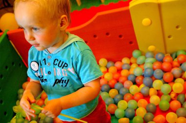 Mavi takımlı küçük bir çocuk küçük renkli toplarla dolu bir top havuzunda oturuyor..