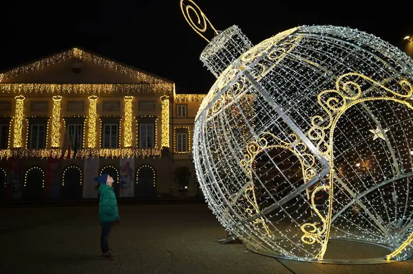 Mutlu Noeller ve mutlu yıllar. Yeşil ceketli kız öğrenci elinde güzel bir Noel süsüsüyle meydanda duruyor. Gece şehrinde büyük bir Noel ağacı balosu şeklinde.