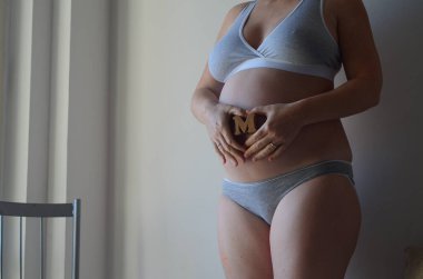 Hamile bir kadın karnında M harfini taşıyan bir erkek bekliyor. Aileyi genişletmek. Annelik