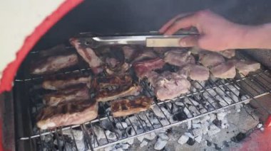 Bahçe barbeküsünde kömürde farklı türde et pişiren bir adamın elleri. Yemek, insan ve aile zamanı kavramı