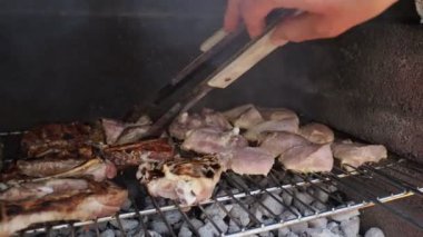 Bahçe barbeküsünde kömürde farklı türde et pişiren bir adamın elleri. Yemek, insan ve aile zamanı kavramı