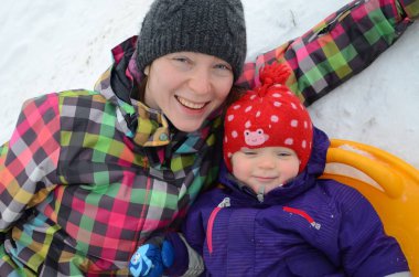 Anne ve küçük kızı karda uzanmış güzel kış günlerinin tadını çıkarıyor. Kış aile aktivitelerinin ötesinde.