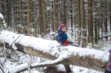 Kış ormanı Devrilmiş bir ağacın gövdesi karla kaplıydı. Sıcak giysili küçük bir çocuk elinde plastik bir çocuk küreğiyle bagajda oturuyor. Bagaja odaklan, çocuk odaklanamıyor.