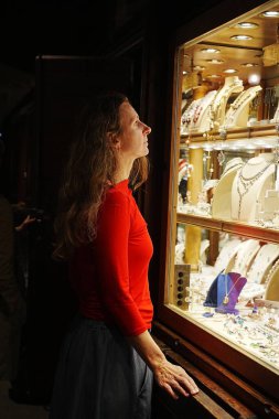 Uzun saçlı bir kadın mücevher dükkanından altın ya da elmas seçiyor.