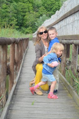 Grandmother with little grandchildren on a wooden path on stilts on the shore of a lake. WWF path as a concept of wildlife conservation clipart