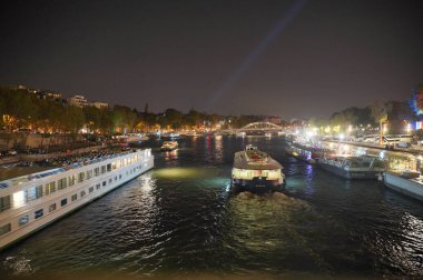 Paris 7 Ekim 2023. Paris 'te geceleri, diğer şenlik tekneleriyle çevrili bir vapur Seine nehri boyunca süzülür. Sahne sıcak sokak lambalarıyla aydınlatılıyor, neşeli ve büyülü bir atmosfer yaratıyor. Seyahat, romantizm ve şehir manzarası temaları için mükemmel