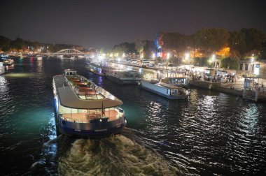 Paris 7 Ekim 2023. Paris 'te geceleri, diğer şenlik tekneleriyle çevrili bir vapur Seine nehri boyunca süzülür. Sahne sıcak sokak lambalarıyla aydınlatılıyor, neşeli ve büyülü bir atmosfer yaratıyor. Seyahat, romantizm ve şehir manzarası temaları için mükemmel