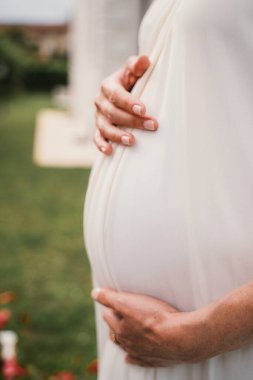 Karnını nazikçe tutan hamile bir kadının yakın plan çekimi. Bakım ve beklenti hissi veriyor. Görüntü hamileliğin güzelliğini ve duygusunu vurgular.