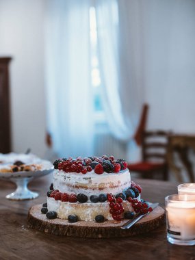 Taze böğürtlenlerle kaplı, ahşap bir masada duran iki katlı bir köy pastası. Yakınlarda, yanan mumlar sıcaklık katar, toplanma ve kutlamalar için ideal sıcak atmosferi geliştirir.