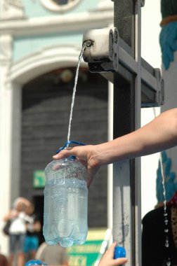 Halka açık bir fıskiyedeki su deresinin altında plastik bir şişe tutan kol. Şişe suyla doluyor, kentsel alanlarda su ve sürdürülebilirliği vurguluyor