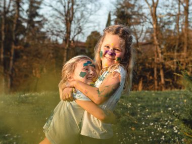 Boyalı yüzlü iki neşeli kardeş, ağaçlarla çevrili doğal bir doğa ortamında sevgi dolu bir kucaklaşmayı paylaşıyor. Mutluluk ifadeleri ve neşe dolu bir zevk sergiliyorlar..