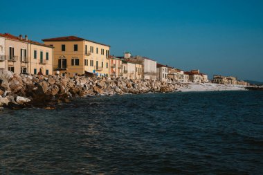Pisa İtalya 29.04 / 2025 Sahil manzaralı sakin deniz kenarındaki kayalık sahilde berrak mavi gökyüzü altında canlı binaları olan bir kasaba. Seyahat, mimari ve turizm konuları için ideal