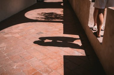 Güneşli tuğla bir yolda öpüşmek için eğilen bir çiftin gölgesi. Sadece bacaklar ve gölgeler görünür, kimlikleri açığa çıkarmadan samimiyet ve samimiyet hissi verir.