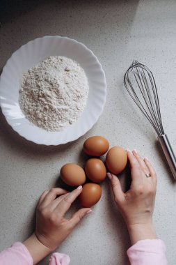 Eller bir kase un ve mutfak tezgahında çırpılmış bir çırpıcının yanına yumurta yerleştiriyor. Bu da pişirme hazırlığını gösteriyor. Sahne ev yemeği aktivitesi olduğunu gösteriyor.