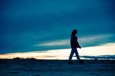 Muhteşem mavi bir günbatımında sahilde yürüyen bir insanın silueti. Bireyler rahat giyinir ve düşünceli görünürler. Huzurlu ve huzurlu bir atmosfer yaratırlar..