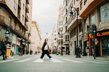 Valencia İspanya 20 Ocak 2024 Şehir Sahnesi 'nde gülümseyen bir kadın karşıdan karşıya geçiyor. Şehir binaları, yayalar ve canlı bir atmosferle çevrili, şehir yaşam dinamiklerini yakalıyor..