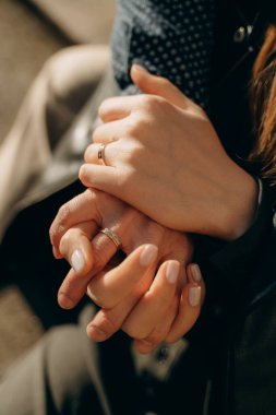 Birbirlerini nazikçe tutan ve yüzüklerini gösteren iki elin yakın plan görüntüsü. Duygu, yakınlık ve bağlantıdır. Sevgi ve ortaklığın altını çizer..