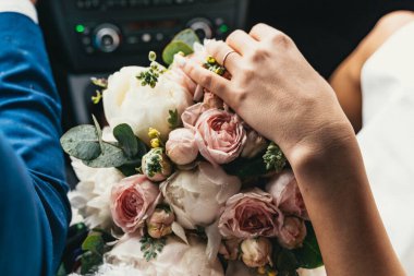 Bir gelin arabada otururken güzel bir buket gül ve şakayık tutar. Görüntü düğün gününün zarafetini ve beklentisini yakalıyor.