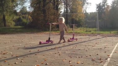 Çıplak ayaklı ve meraklı bir çocuk, iki pembe scooterlı bir sonbahar parkını keşfediyor. Düşen yapraklar ve ağaçlarla çevrili sahne, neşeli keşif ve masumiyetin özünü yakalıyor.