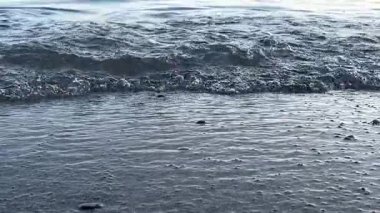 Yumuşak dalgalar yumuşak kumlu kıyıya ulaşarak sakin ve huzurlu bir sahil manzarası yaratıyor. Suyun ritmik hareketi deniz kenarında sakin bir an sunuyor, sakinliği çağrıştırıyor.