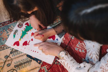 Çocuklar renkli bir Noel temalı sanat eserini keçeli kalemlerle kağıda dökerek yaratıcı bir çizim faaliyetinde bulundular. Etkinlik, tatil ruhunu gösteren desenli bir halının üzerine kurulmuş.