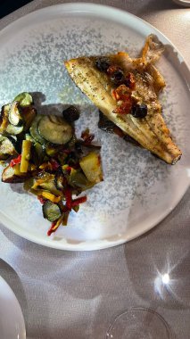 Renkli, ızgara sebzelerle servis edilen kızarmış balık filetosu. Tabakta güzel bir şekilde hazırlanmış, sağlıklı ve lezzetli bir yemek seçeneği sunuyor.