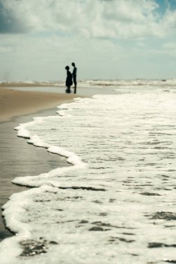 İki kişi sahile vuran dalgalarla sakin bir sahil boyunca yürür. Sahne, okyanusun sesi ve ayak altında kum hissi ile huzurlu bir anı yakalar..