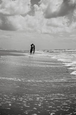 Bir çift, sakin bir plajda samimi bir kucaklaşmayı paylaşıyor. Siyah ve beyaz tonlar romantik ve barışçıl atmosferi güçlendirir, bir bağ ve aşk anını yakalar..