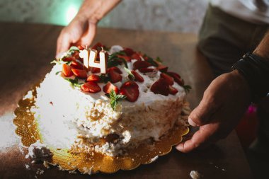 Eller dikkatlice masaya 14. yaş günü pastasını yerleştiriyor. Taze çilek ve mumlarla süslenmiş. Tatlı tatlı, şen ve neşeli bir kilometre taşı kutlaması sergiliyor.
