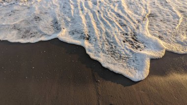 Kumlu bir kumsalda dalgaların dalgalanma ve köpük oluşturduğu yakın çekim görüntüsü..