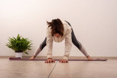 Bir kadın bitkinin önündeki mindere yoga pozu veriyor. Poz aşağı bakan bir köpek, ve kadın ellerine bakıyor. Sakinlik ve odaklanma kavramı