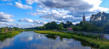 Nehrin üzerindeki kilise bulutlu havalarda yeşilliklerle çevrili ve su yüzeyine yansıyan bulutlarla dolu. 