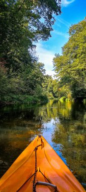 Güneşli bir günde ormanın yakınındaki bir nehirde kano kullanmak nehrin kenarından çekilir. Yaz sporları. Aktif yaşam tarzı. Widawka Nehri