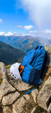 Hiking backpack for travel and helmet for climbing mountains. Traveling in the mountains. Hiking in the High Tatras. Hiking in the mountains as a lifestyle. Mountain climbing equipment. Halt on the mountain road. Vertical photo clipart