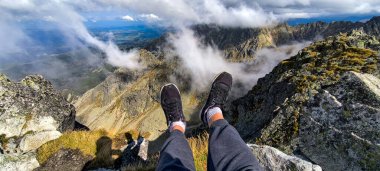 Genç kadın fethedilmiş bir dağın tepesinde oturuyor. Favori bir hobi olarak dağlarda yürüyüş yapmak. Aktif yaşam tarzı. Yürüyüş patikalarından Tatra Dağları ve Yüksek Tatralar 'ın manzarası. Dağlar arasındaki dağ zirveleri, yamaçlar ve vadiler