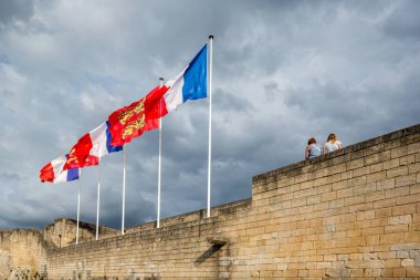 Bayrakların dalgalandığı manzara ve Fransa 'nın Normandiya kentindeki Caen Kalesi' nin antik duvarında oturan insanlar. Bulutlar gökyüzünü dolduruyor, görkemli bir atmosfer yaratıyor..