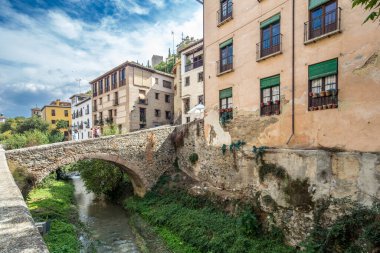 İspanya 'nın Granada kentindeki Darro Nehri üzerindeki tarihi binaların ve taş köprünün manzaralı manzarasında eski dünya cazibesi ve manzaralı bir çevre sergileniyor..