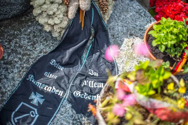 stock image Close-up of a Waffen SS memorial ribbon at the German military cemetery in Normandy, France, surrounded by vibrant flowers and stone artifacts.