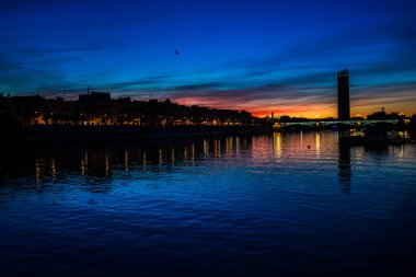 Triana Köprüsü ve aydınlatılmış Betis Caddesi, Sevilla, İspanya 'nın yer aldığı Guadalquivir Nehri üzerinde gün batımı manzarası.