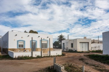 Almerya kırsalında bulutlu bir gökyüzünün altında mavi panjurlu beyaz kübik evler.